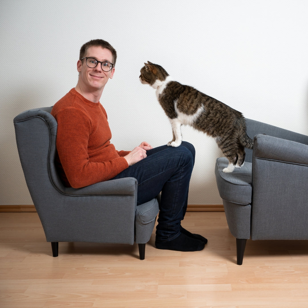 Man sitting on a gray chair with a cat standing on another chair